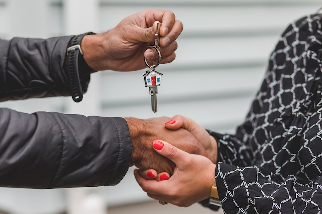 Two people shaking hands, one of them is holding up a key 